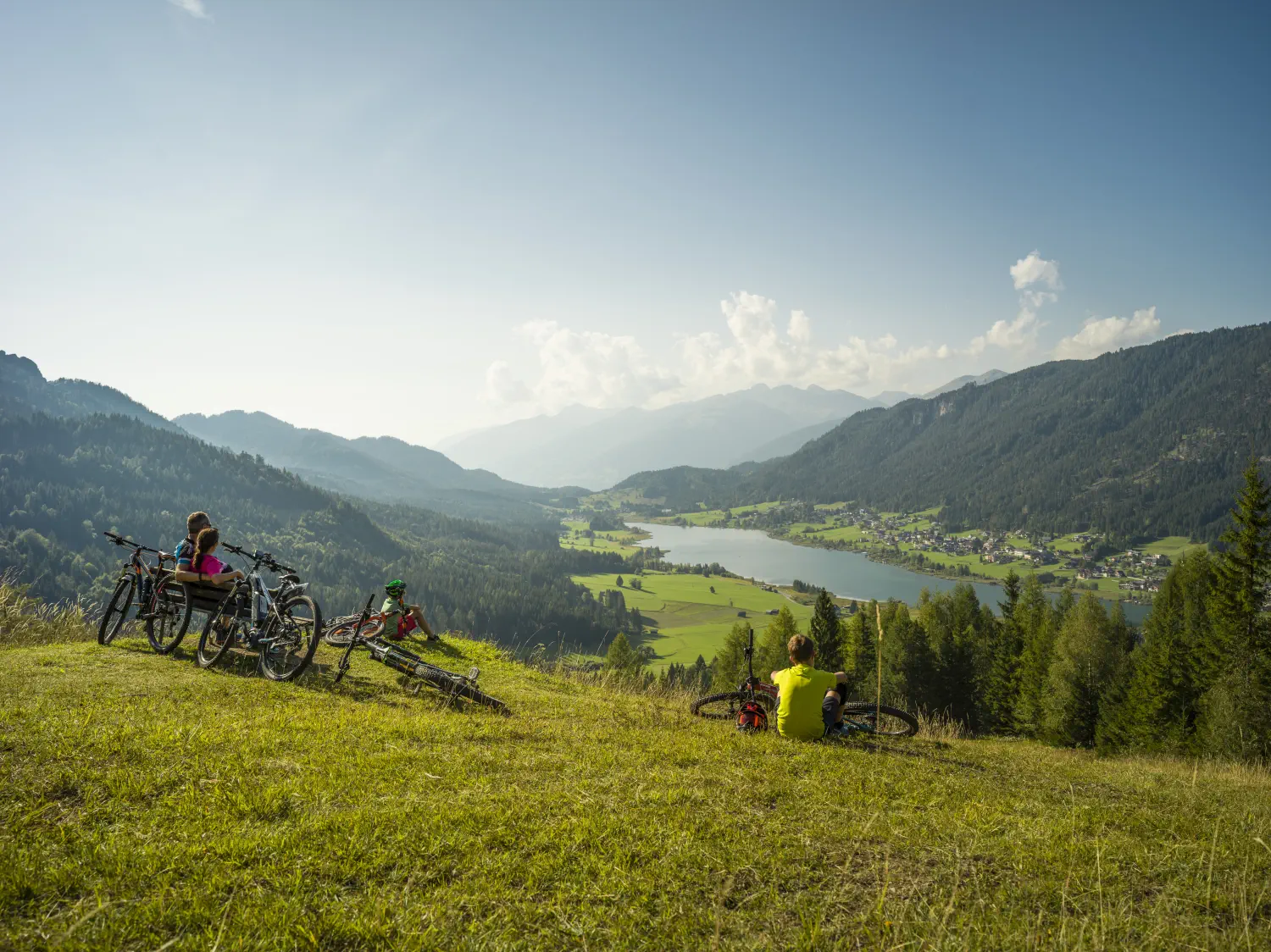 Eine Familie blickt nach der Radtour zufrieden vom Berg hinunter auf den Weissensee